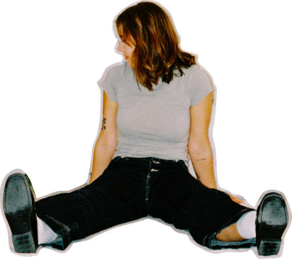 A cutout of
		  Lea sitting on the floor in a child-like pose, with her legs out, and
			looking off to the side. She is wearing a grey short-sleeve top, black
			pants, and black shoes. She has long, brown, wavy hair which hangs over
			the side of her face, covering most of her face from view. A couple of
			tatoos can be spotted on her arms.